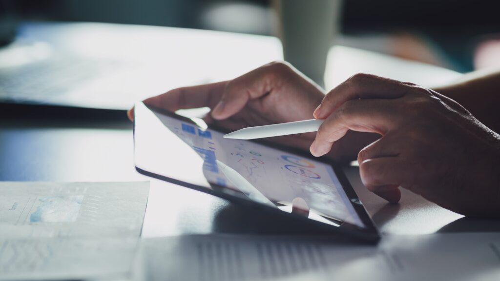 Hands holding a stylus and a tablet. Graphs are displayed on its screen.