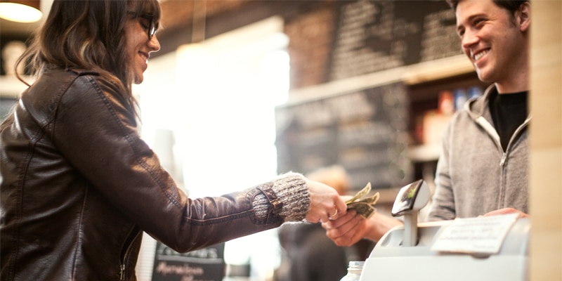 A photo of a woman paying cash to a man behind a register.